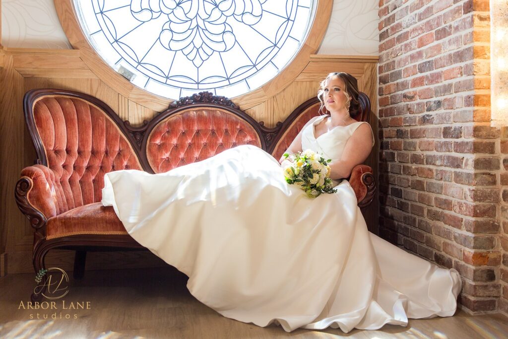 a bride sitting on a red chair in front of a round window