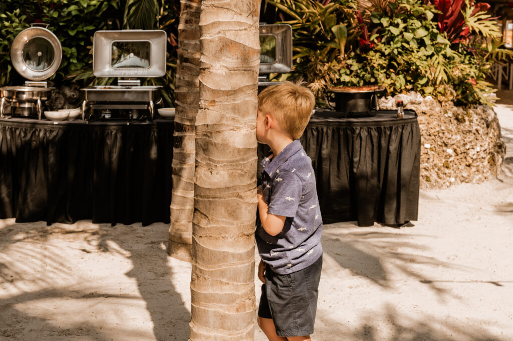 a young boy standing next to a palm tree