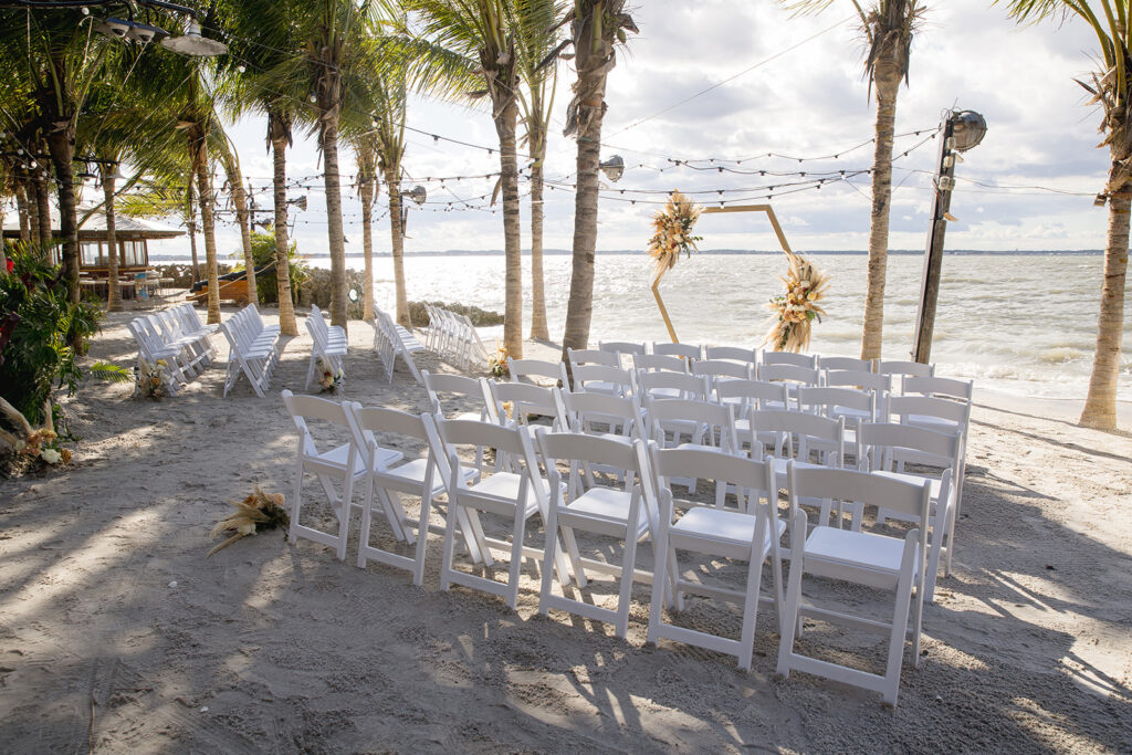 a row of white chairs sitting on top of a sandy beach